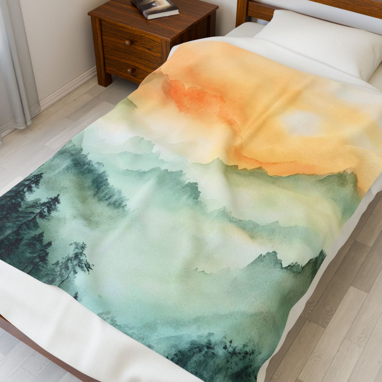 Soft blanket with watercolor mountain and sunrise design draped on a bed in a cozy bedroom.