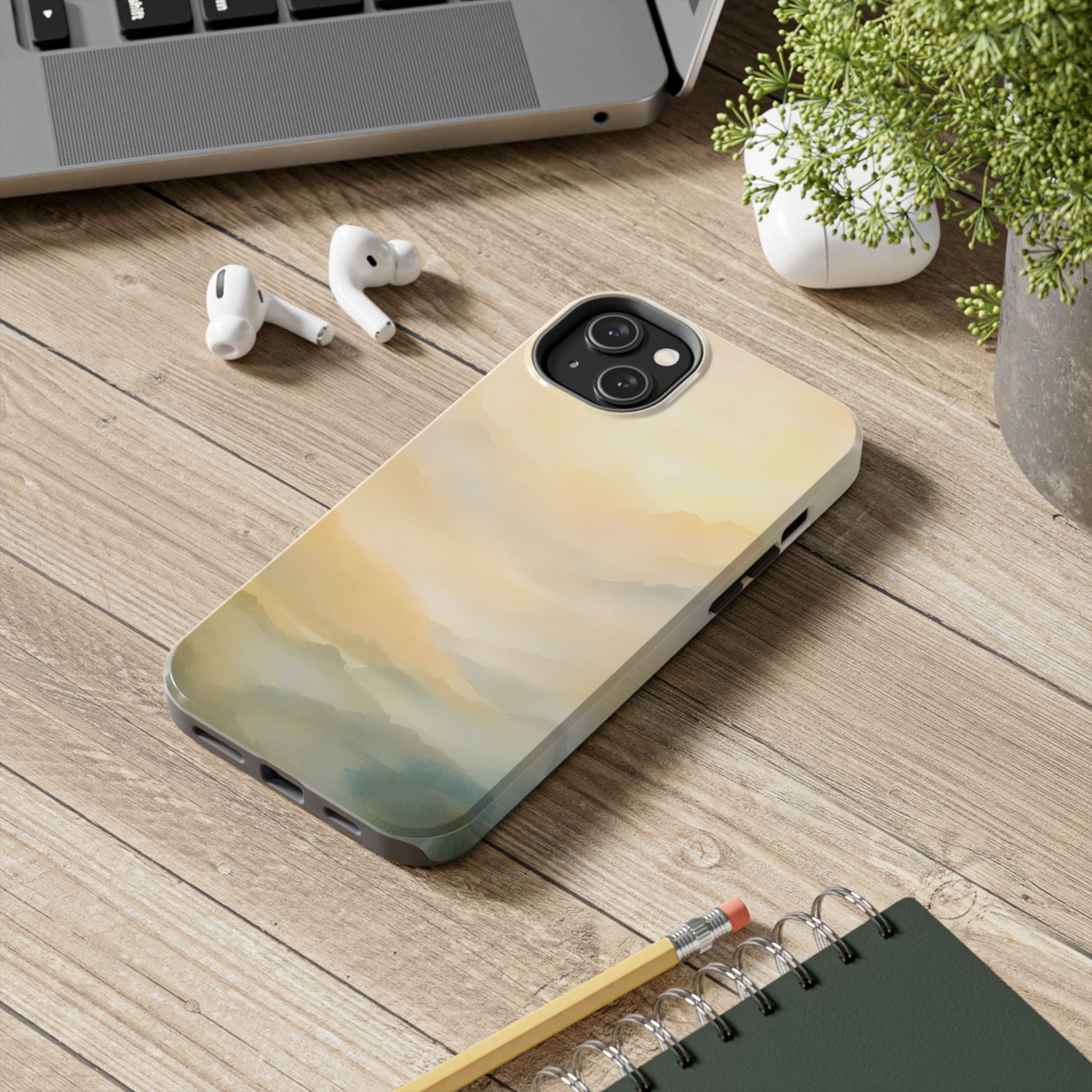 Abstract mountain sunrise phone case on wooden desk with earbuds, plant, and notebook