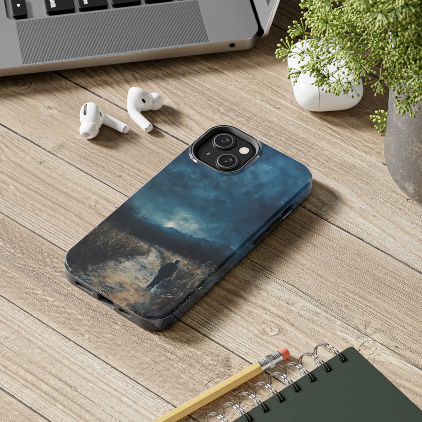 Phone case with contemplative landscape art of a figure on a path, shown on a wooden desk.