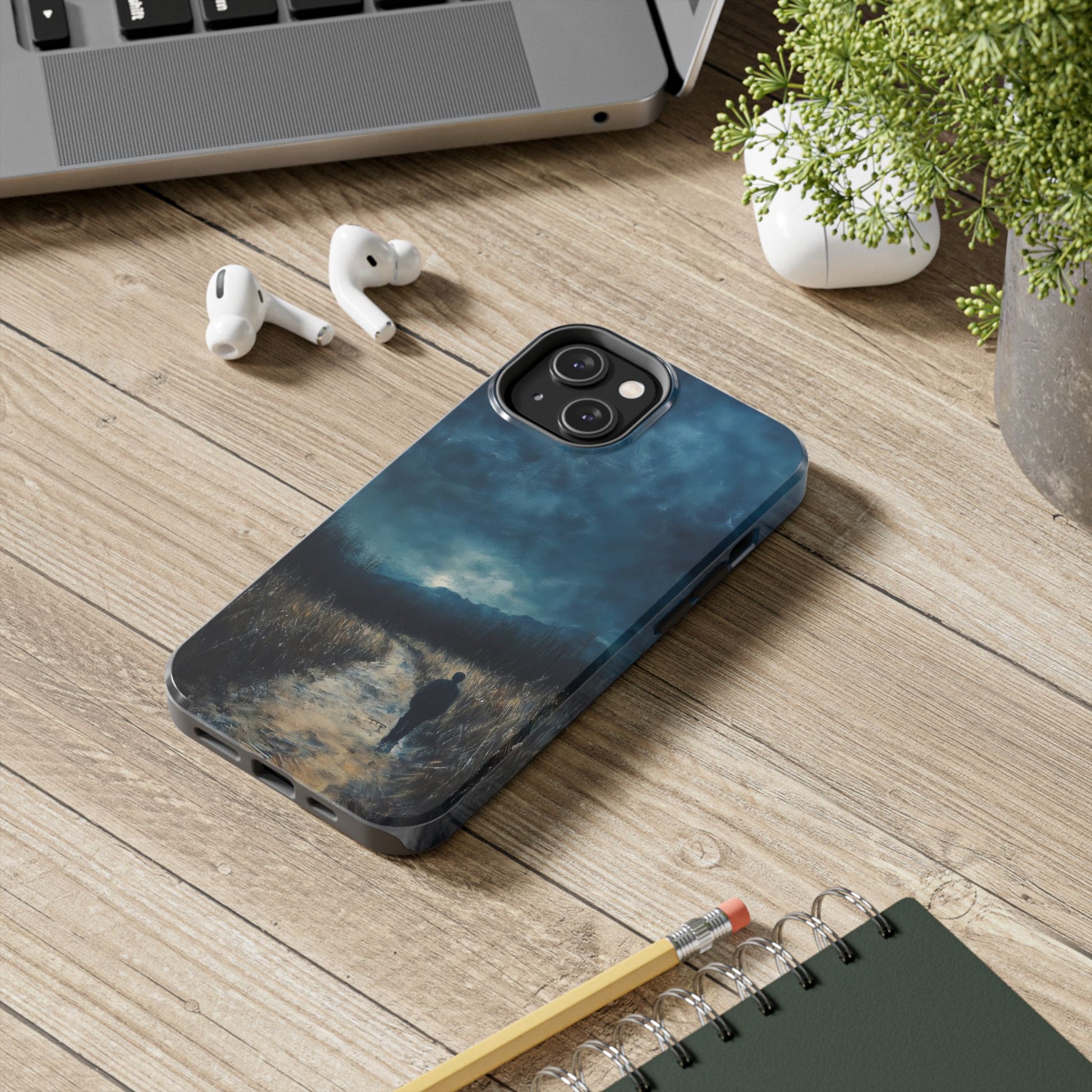 Phone case with contemplative landscape art of a figure on a path, shown on a wooden desk.