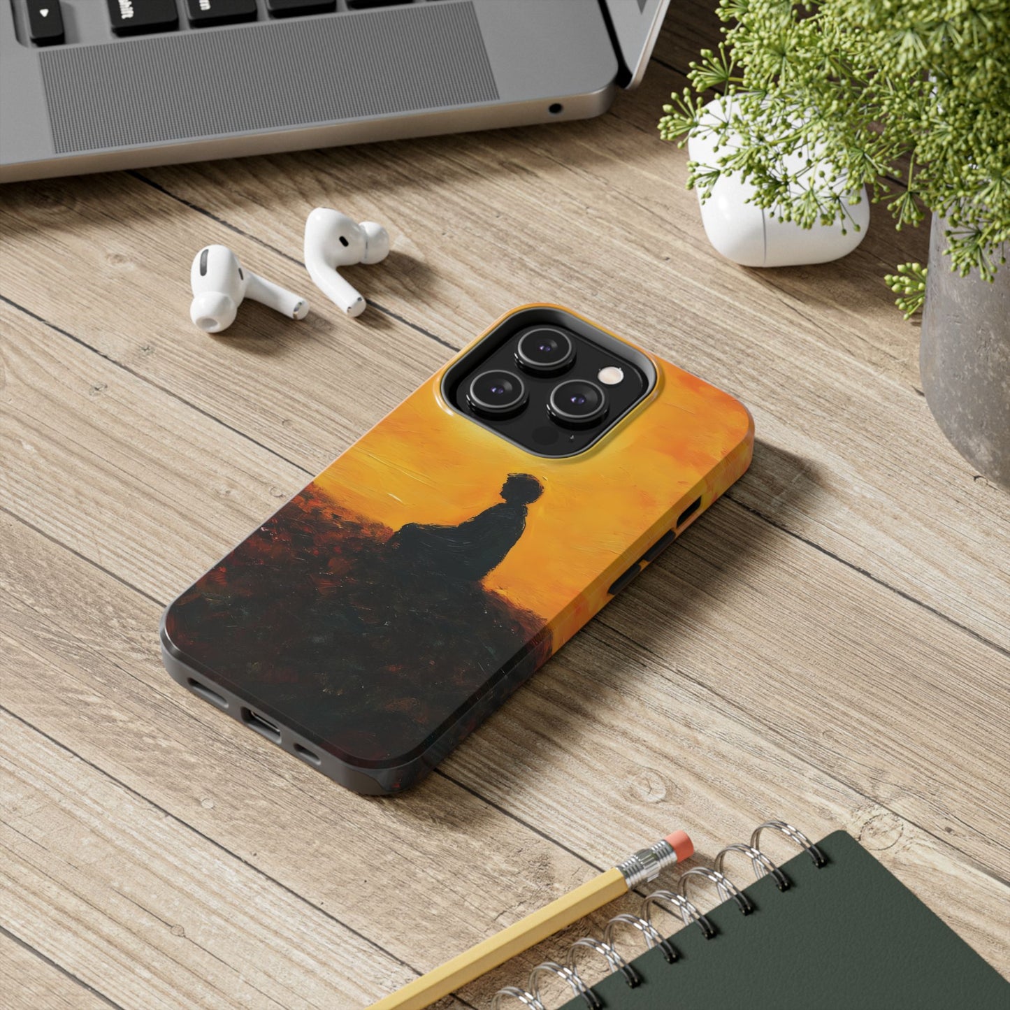 Phone case with meditative silhouette against orange sunset, on wooden desk with earbuds and laptop