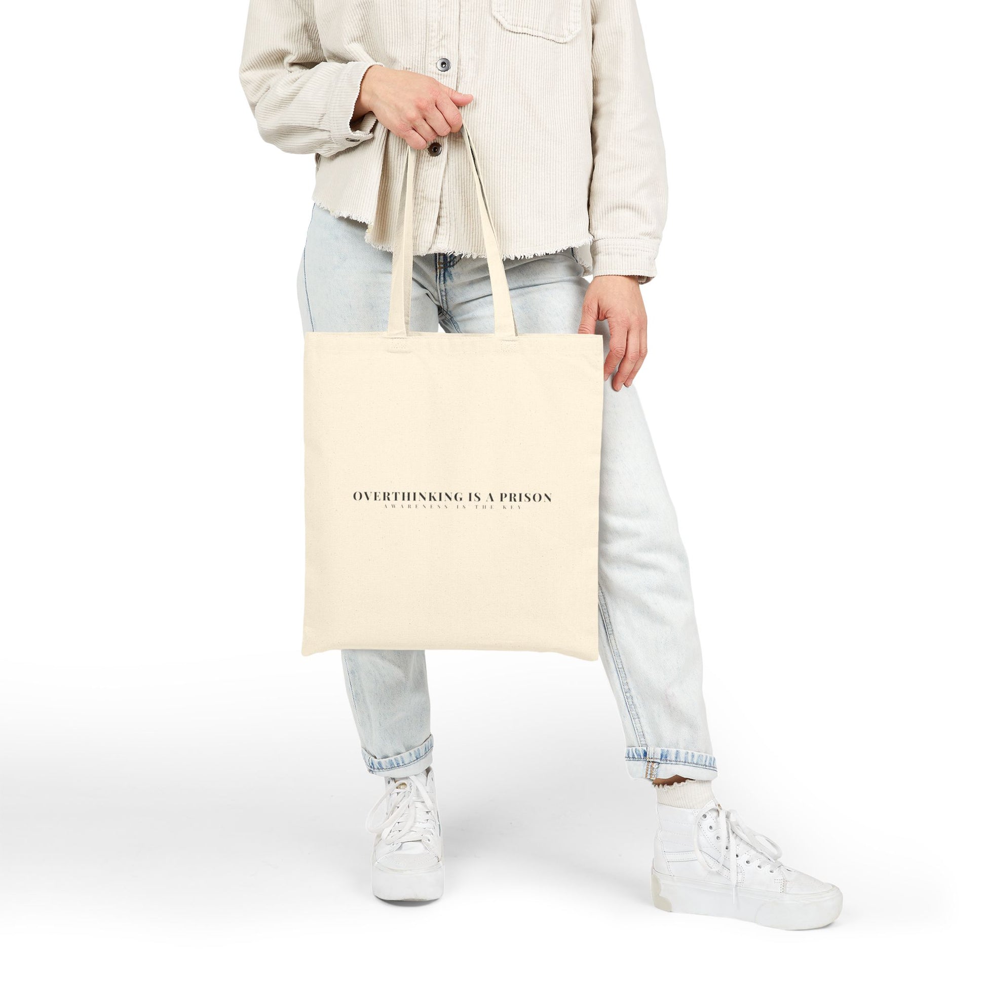Person holding beige tote bag with 'Overthinking is a prison' motivational quote, casual outfit