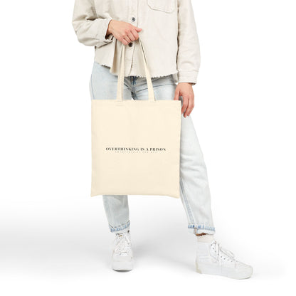 Person holding beige tote bag with 'Overthinking is a prison' motivational quote, casual outfit