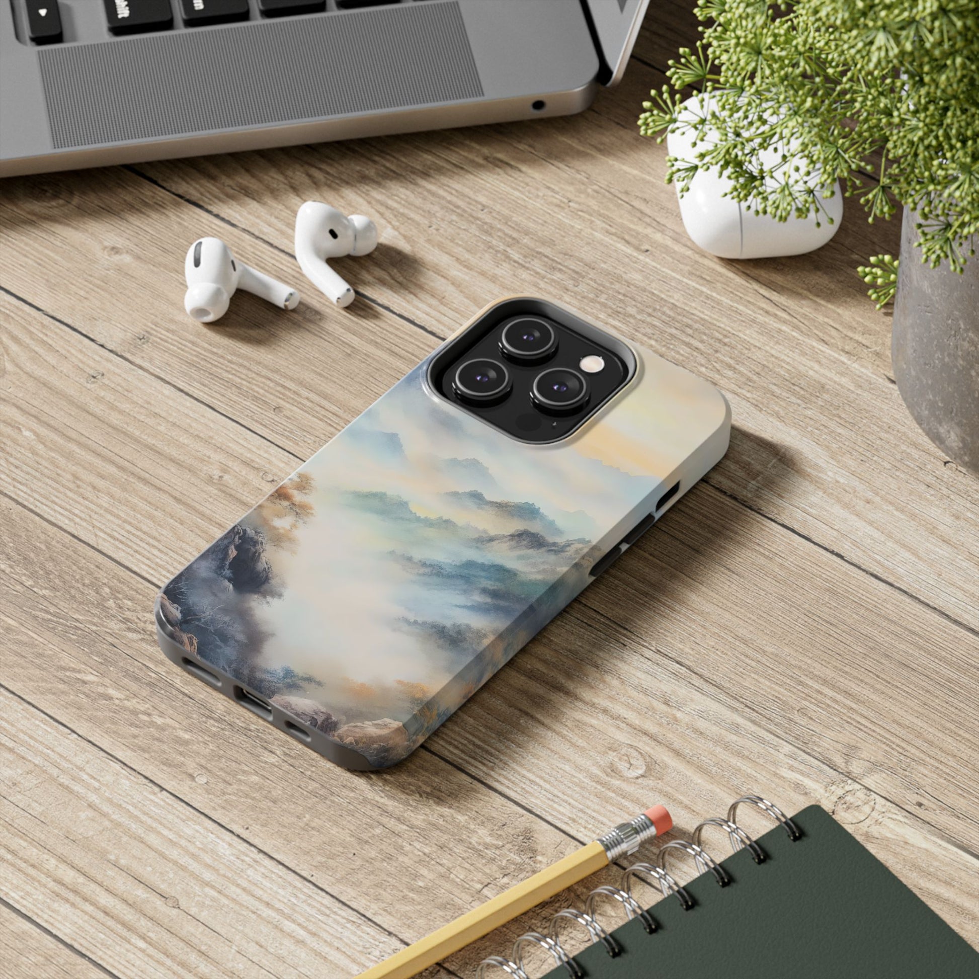Phone with serene mountain landscape case on wooden desk with earbuds and laptop
