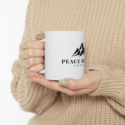 Woman in beige sweater holding white mug with mountain graphic and 'Peace Beyond Thought' text