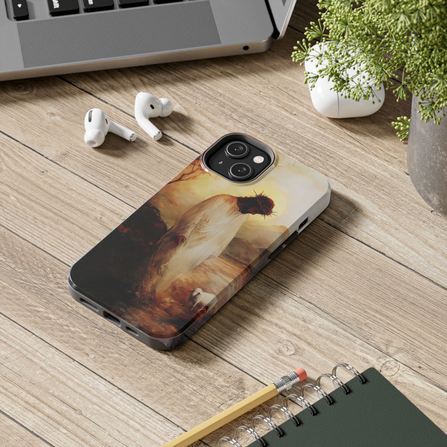 Christian phone case with Jesus art, crown of thorns, and lamb on wooden desk with laptop