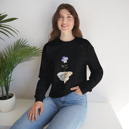 Woman wearing black sweatshirt with purple flower and rock graphic, sitting by potted plant
