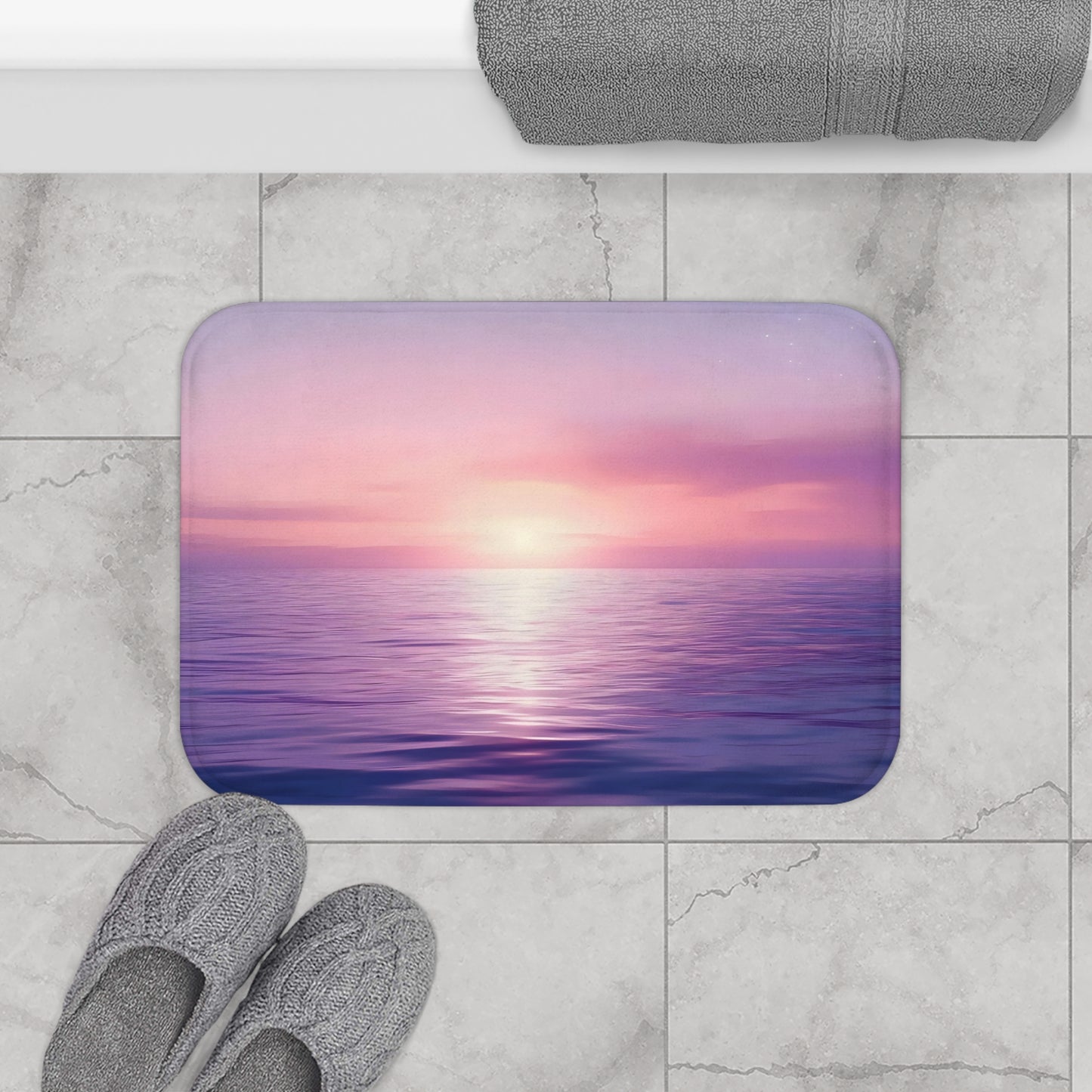 Bathroom mat with serene purple and pink ocean sunset, gray slippers, and towel on tile floor