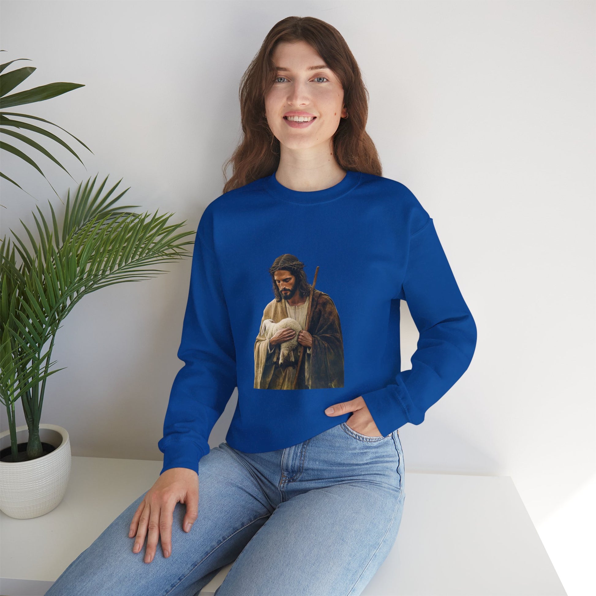 Woman wearing blue Christian sweatshirt with shepherd and lamb graphic, sitting indoors by plant