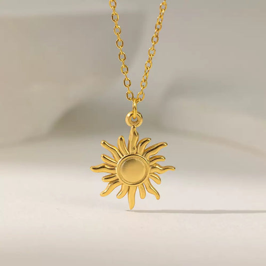Gold-tone sun-shaped pendant and fine chain on a pale background